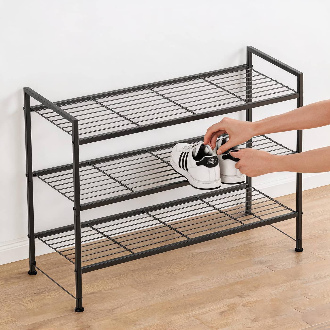 Person placing a shoe on a black three-tier rack